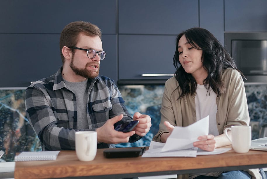 Couple sitting at desk with coffee, calculator and paperwork discussing taxes