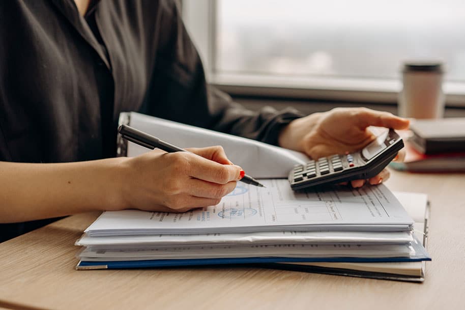 Image of woman with stack of papers and calculator filling out the paperwork