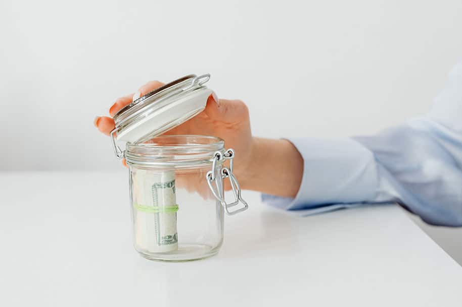 Image of person closing mostly empty glass jar with one roll of bills