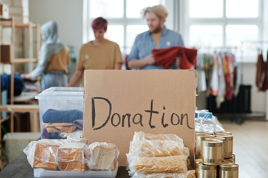 A Cardboard with Inscription that says donation, with food donations surrounding it.