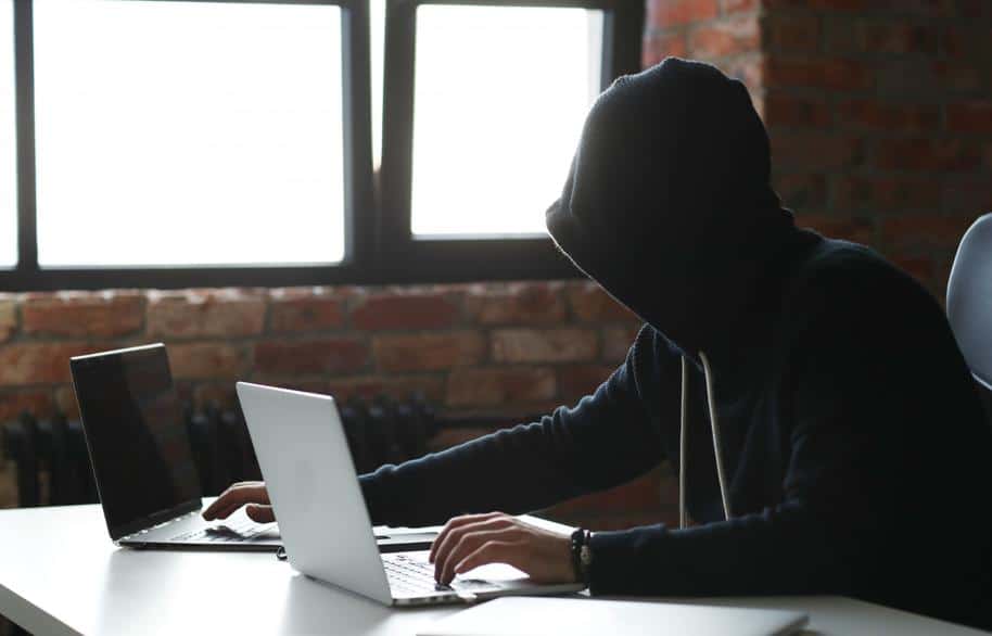 Man wearing hoodie using two laptops