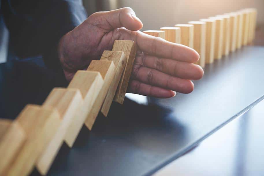 Closeup of a hand stopping a line of falling dominoes.