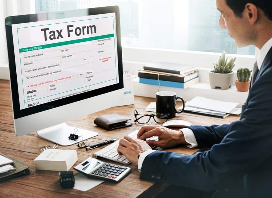 Man in a suit filling out a tax form on his desktop computer monitor.